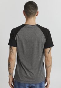 Camiseta de manga corta con cuerpo gris y mangas raglán negras. Fabricada en algodón, tiene una textura suave y un corte clásico.