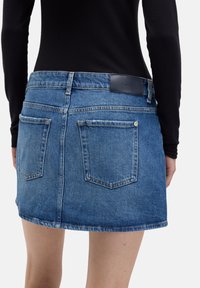 Blaue Denim-Minirock mit ausgefranstem Saum, zwei Gesäßtaschen und einem markenprägenden Lederetikett am Taillenbund.