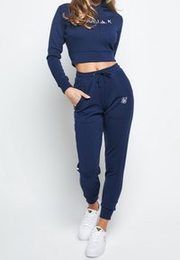 Námořnická modrá cropped mikina s kapucí a bílým logem, spárovaná s odpovídajícími tepláky se svislými pruhy a elastickými manžetami.