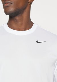 Camiseta blanca de Nike con cuello redondo, que presenta un pequeño logo negro en el lado izquierdo del pecho. Tela suave y ligera con un diseño ajustado.