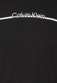 Schwarzes Baumwoll-T-Shirt mit einem weißen "Calvin Klein"-Logo und einer geschwungenen weißen Linie über dem Text. Weicher Stoff mit klassischer Passform.