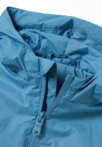 Giacca blu chiaro con colletto alto, chiusura frontale con zip e texture liscia. La fodera è visibile con morbide pieghe.