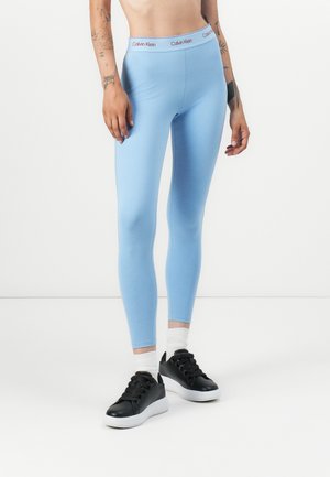 Lichtblauwe leggings met een aansluitend ontwerp en een elastische tailleband met 'Calvin Klein' logo in het rood. Gedragen met zwarte sneakers.
