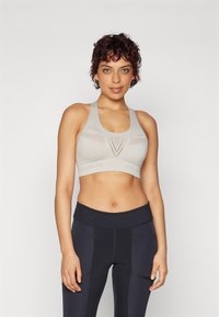 Jasnoszary sportowy crop top z teksturowanym wzorem i szerokimi ramiączkami, w połączeniu z czarnymi legginsami nawysokim stanie z bocznymi kieszeniami.