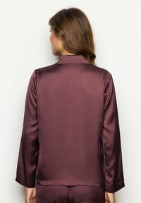 Blusa de satén burdeos con mangas largas, cuello tipo solapa y una textura suave. La prenda presenta un diseño simple y limpio.