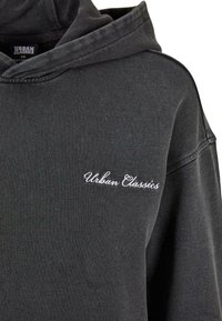 Felpa grigia scura con "Urban Classics" ricamato in bianco corsivo sul lato sinistro del petto e un cappuccio sul retro.