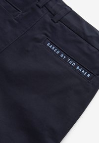 Kara jūras zilas auduma bikses piedāvā elegantu dizainu ar gludu tekstūru. Aizmugurējā kabatā ir taisnstūra etiķete ar uzrakstu "BAKER BY TED BAKER".