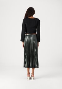 Black cropped long-sleeve top paired with a pleated metallic green skirt. Skirt features vertical pleats and a smooth texture, with heels visible.