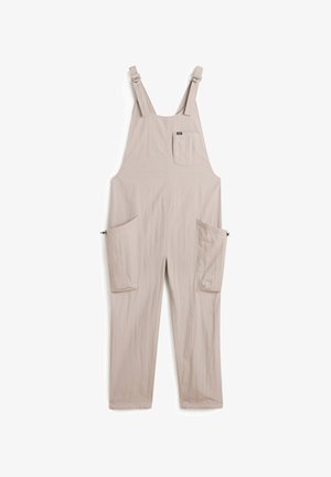 Overoles beige hechos de una tela ligera con tirantes ajustables, un bolsillo en el pecho y dos grandes bolsillos laterales para almacenamiento.