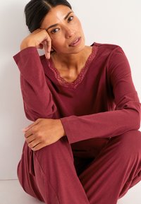 Maroon loungewear-set med lång ärm och byxor, med V-ringning med spetsdetaljer. Mjuk tyg och en avslappnad passform med slät textur.