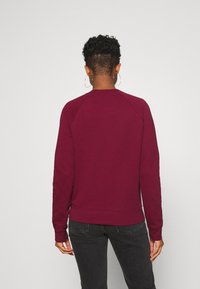 Burgundier sweatshirt med långa ärmar och rundad halsringning, med ribbat fåll och ärmslut. Slät textur, med raglanärmar.