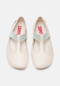 Beige leather shoes with rounded toes and cutout design, featuring a light blue elastic strap across the instep and red branding inside.