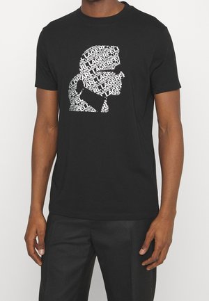 Personne portant un t-shirt noir avec un motif blanc d'une silhouette de profil latéral composée du texte répété "KARL LAGERFELD".