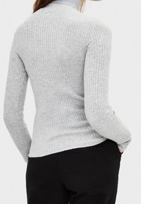 Pull à col roulé gris côtelé avec une coupe ajustée et des manches longues, présentant un tissu texturé et un design dos sans coutures.