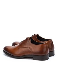 Une paire de chaussures de ville pour hommes en cuir marron poli avec des lacets et des semelles noires sur un fond blanc.
