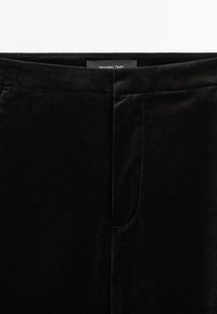 Pantalons en velours noir avec une texture lisse, un léger éclat, des poches avant et un design minimaliste. Marque : Massimo Dutti.