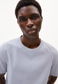 Hellgraues Baumwoll-T-Shirt mit Rundhalsausschnitt und kurzen Ärmeln, das eine glatte Textur und ein minimales Design aufweist.