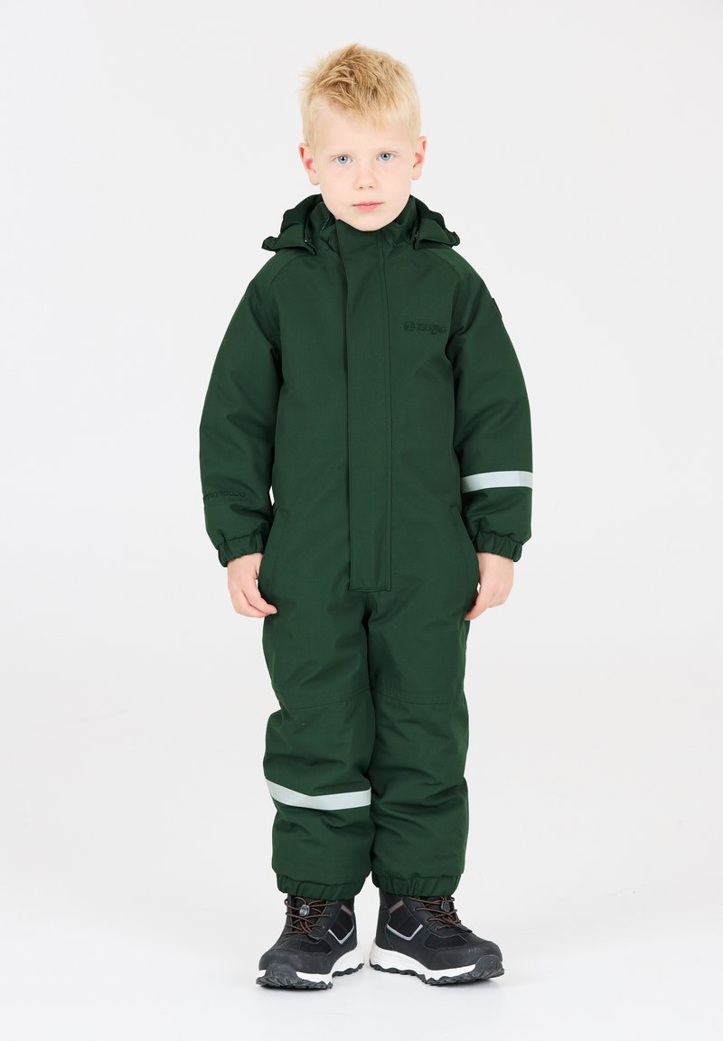 Groene waterdichte overall met een rits aan de voorkant, elastische manchetten en reflecterende accenten. Gecombineerd met zwarte waterdichte laarzen.