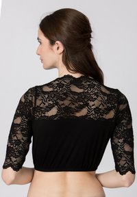Schwarzes Crop-Top mit komplizierten Spitzenschultern und tailliertem Oberteil. Die Spitze hat ein florales Muster und gewellte Kanten.