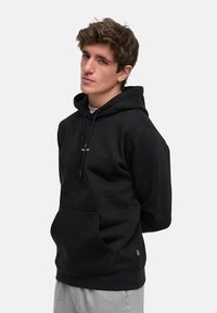 Svart hettegenser med frontlomme og snøring i hetta. Enkelt design med en liten logo på brystet. Mykt materiale, avslappet passform.