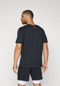 Schwarzes Performance-T-Shirt mit kurzen Ärmeln, Rundhalsausschnitt und kleinem Logo auf dem Rücken. Das Material wirkt glatt und leicht.