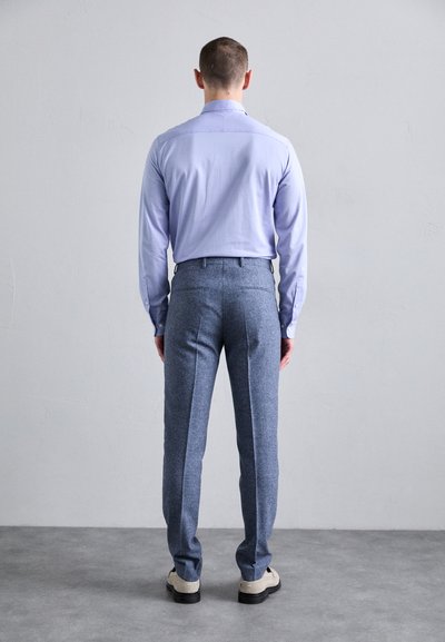 Cămașă lungă cu mânecă închisă, de culoare mov deschis, cu o textură netedă, asociată cu pantaloni din lână gri, cu un finisaj texturat și croială ajustată.
