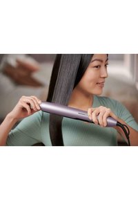 Haarstraighter mit einem eleganten, metallischen lila Gehäuse, ausgestattet mit einem digitalen Display und strukturierter Grifffläche, die durch glattes, glänzendes Haar gleitet.