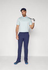 Light blue polo shirt with short sleeves, navy trousers, blue athletic shoes, and a blue cap, holding a golf club with a gloved hand.