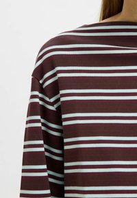 Triibuline t-särk, millel on laiad horisontaalsed triibud burgundi ja mündirohelise värviga, lõdva lõike ja siledalt pehme tekstuuriga.