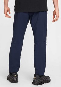 Navyblauwe outdoorbroeken met een gladde textuur, taps toelopend ontwerp en gestikte accenten, gecombineerd met zwarte sportschoenen met zichtbare branding.