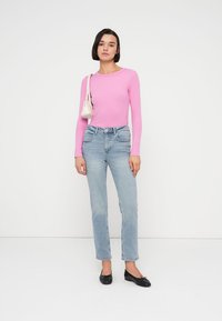 Ροζ ανοιχτό ροζ μακρυμάνικη εφαρμοστή μπλούζα, μπλε ψηλόμεσα τζιν με ίσια μπατζάκια, μαύρα μπαλαρίνα παπούτσια και μικρή λευκή τσάντα.