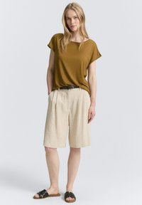 Top marrone a maniche corte abbinato a pantaloni corti plissettati beige e sandali neri. L'outfit presenta una vestibilità comoda e un design semplice.