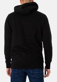 Sudadera con capucha negra de algodón, con una textura suave y un ajuste relajado. La capucha tiene una forma redondeada, con puños y dobladillo acanalados.