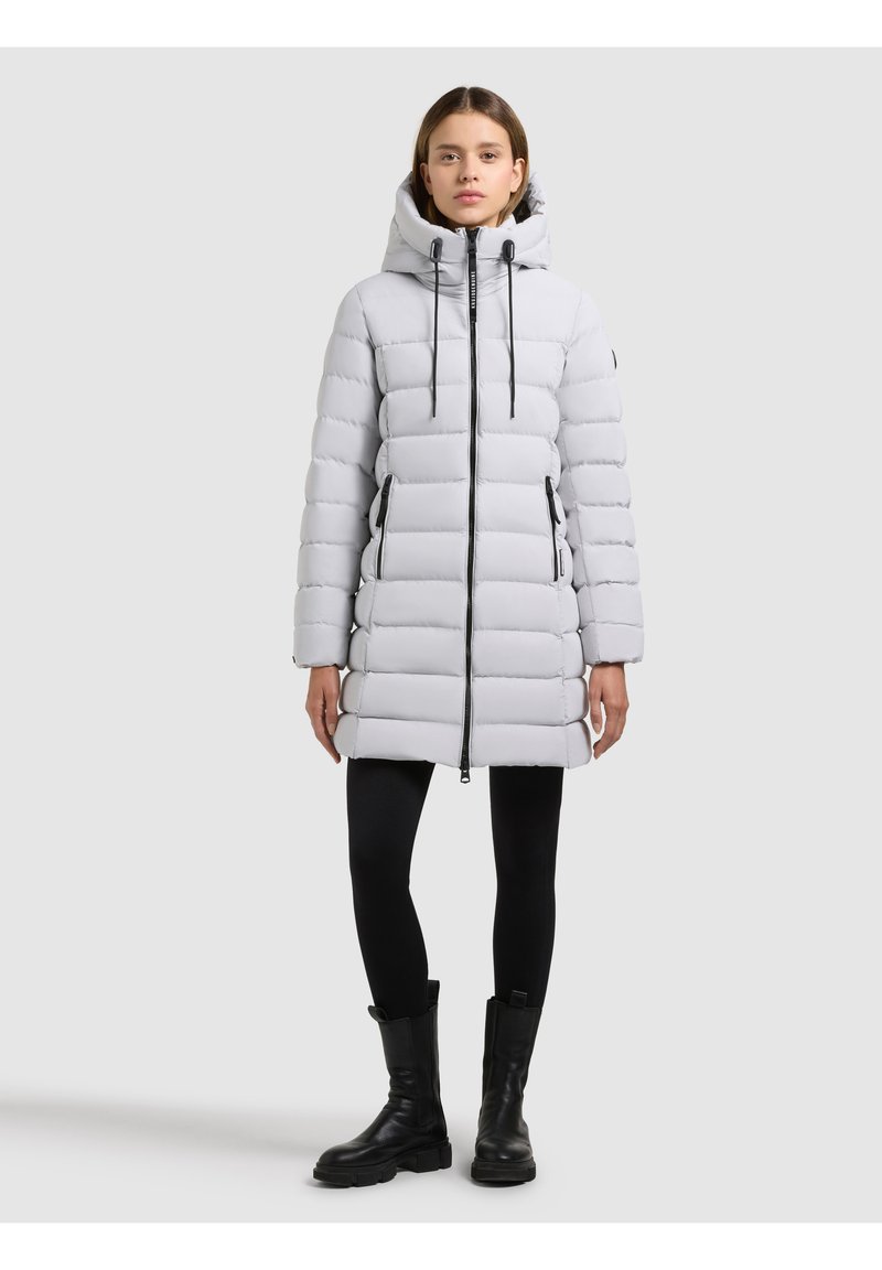 Ljusgrå vadderad jacka med horisontella sömmar, dragkedja fram, dragsko i huvan och två sidofickor. Bärs över svarta leggings och stövlar.