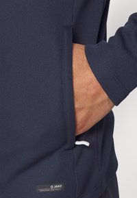 Het marineblauwe sportshirt heeft een zijvak, lichte stiksels en een klein logo-label. De stof ziet er soepel en vochtregulerend uit.