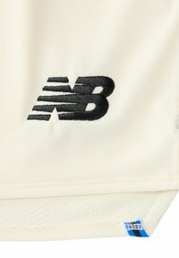 Roomkleurig sportshirt met een gestructureerd oppervlak, voorzien van een opvallend zwart geborduurd "NB"-logo en een blauwe accentlabel aan de zoom.
