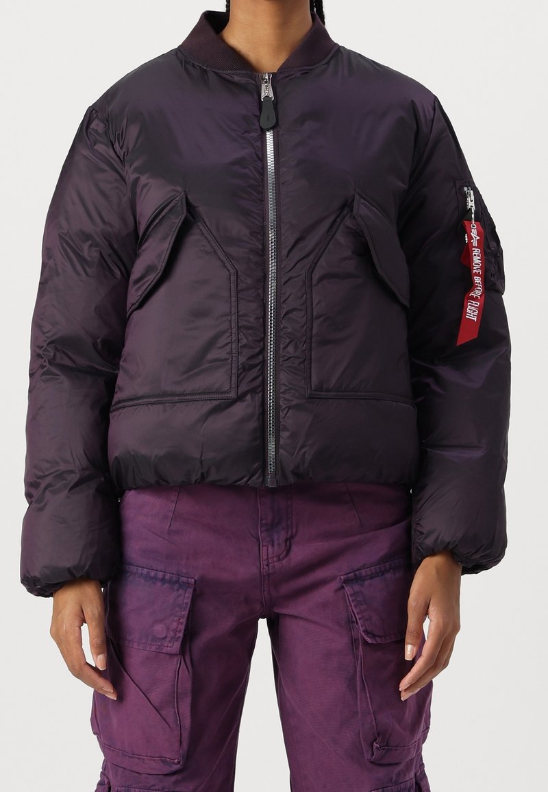 Personne portant une doudoune violet foncé avec poches avant et un pantalon cargo violet avec poches à rabat boutonnées.