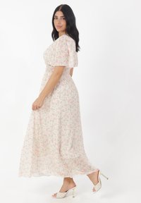 Sukienka maxi z lekkiego materiału w różowo-zielony kwiatowy wzór. Posiada krótkie bufiaste rękawy oraz dopasowaną talię, zestawiona z lekkimi butami na obcasie.