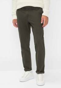 Pantaloni in cotone verde oliva con vestibilità slim e orli arrotolati, abbinati a sneaker bianche. Il materiale ha una texture liscia e una leggerissima lucentezza.