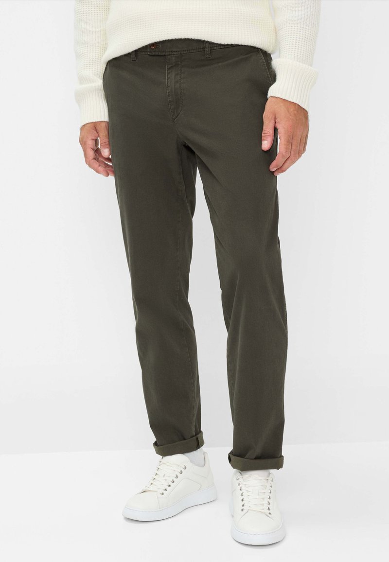 Pantaloni in cotone verde oliva con vestibilità slim e orli arrotolati, abbinati a sneaker bianche. Il materiale ha una texture liscia e una leggerissima lucentezza.