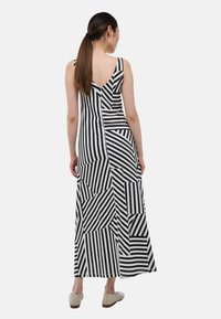 Robe maxi avec un motif géométrique en rayures noires et blanches, dotée d'un large décolleté en V dans le dos, présentant des rayures de largeurs et d'angles variés.
