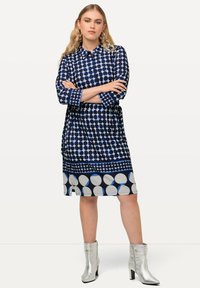 Abito da donna in stile navy con motivo a pois in diverse tonalità di blu. Presenta una chiusura con bottoni sul davanti, maniche lunghe e una lunghezza poco sopra il ginocchio.
