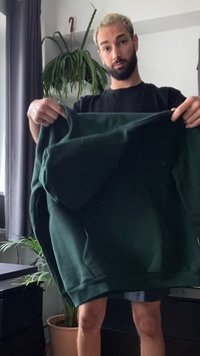 Sweatshirt verde escuro com um corte amplo e tecido espesso. A parte frontal possui um grande bolso com uma textura suave e punhos canelados.