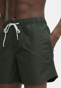 Costume da bagno verde scuro realizzati in tessuto leggero, con vita elastica, cordino bianco e tasche laterali.