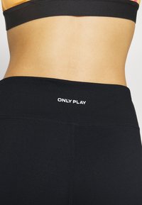 Leggings negros con una textura suave, cintura alta y logo "ONLY PLAY" en blanco en la parte superior de la espalda. Diseño simple, sin patrones.