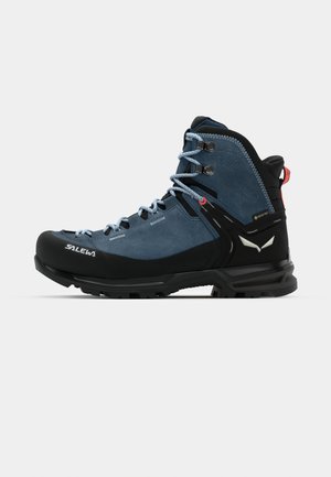 Blå kvalitetssko for fotturer med svart gummisåle, forsterket tå, metall-lissekroker og teksturerte detaljer. Har vanntett Gore-Tex-fôr.