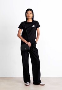 T-shirt crop nera con logo bianco, pantaloni larghi neri, borsa a tracolla nera e sneaker argento con suola marrone. Texture lisce.