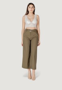 Bralette in pizzo bianco con bordi ondulati, abbinata a pantaloni a vita alta e gamba larga in verde oliva con una fibbia argentata.
