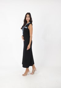Zwart geribbeld maxi-jurk met denim accenten, kapmouwen en een rits aan de voorkant. Gemaakt in combinatie met doorschijnende sandalen met blokhak.