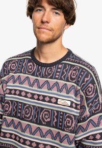 Knit sweater with a geometric pattern in shades of purple, blue, green, and black. Features a round neck and a small logo patch.